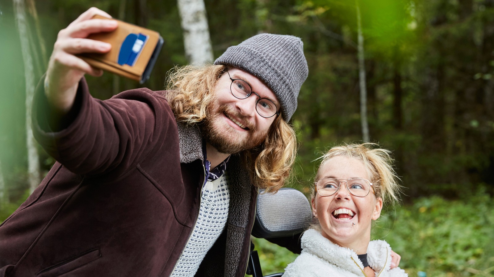 Ung manlig vårdare tar selfie med kvinna i rullstol i skog