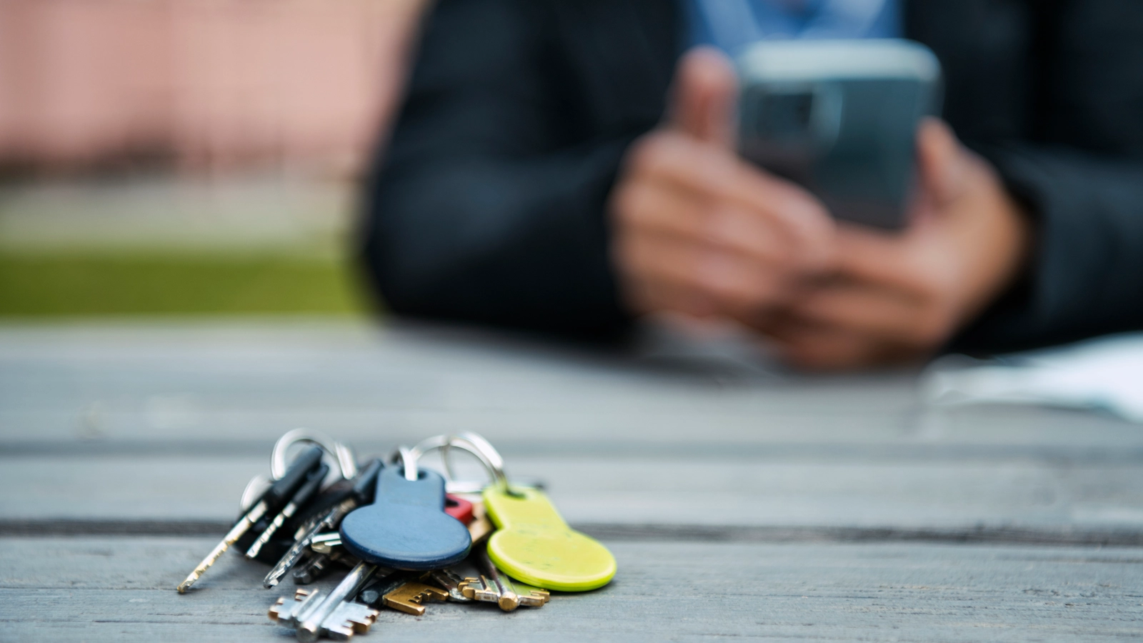 Kvinnlig hemtjänstpersonal tittar på mobil utanför flerfamiljshus och nycklar på bord